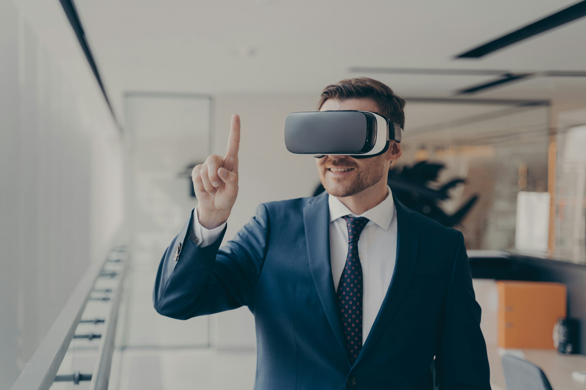 Smiling bearded office employee in suit wearing in VR glasses working in augmented reality in office